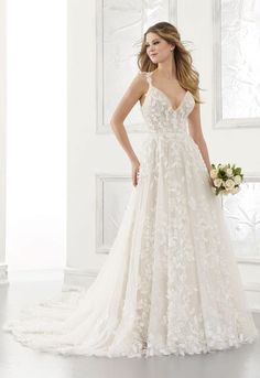 a woman in a wedding dress standing next to a white wall with flowers on it