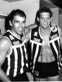 two men standing next to each other in front of a mirror wearing striped vests