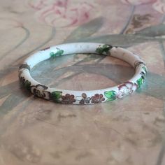 This is a vintage cloisonne bracelet. It is white floral with gold trim. This piece has a hinge and pulls open. There is a chip in the bracelet as you can see in the images as well as specks/pockmarks on the piece. The price reflects this. All sales are final.  The bracelet measures a hair under 2.5 inches across on the interior.  If you have a wish list or are looking for something specific, please ask. I may have exactly what you are looking for. As always please convo me with any questions or concerns regarding this item or with any international shipping questions. Unfortunately I do not accept returns or grant refunds. All shipping fees include handling fees. If you would like to combine shipping costs for more than one item, I would be happy to do so if you convo me before purchase. Collectible White Bracelet Jewelry, Antique White Bracelet Jewelry, White Antique Bracelet Jewelry, White Antique Bracelet, Vintage Hand Painted Bracelets As Gift, Adjustable White Vintage Bangle, Vintage Enamel Bangle As A Gift, Vintage Enamel Bangle For Gift, Vintage Enamel Bangle As Gift