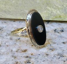 Metal: Solid 14k Yellow and White Gold Stone: 9x18 mm Onyx and a 2mm Diamond Size: 5 Weight: 3.7 grams Era: 1930's This classy ring is white gold on the top and yellow gold on the bottom. Intricately engraved white gold leaves adorn each side of the ring. The oval onyx has a small diamond set in white gold in the center. All of the engraving is still crisp and detailed after all these years. The stone is in very good condition with no eye visible flaws. The interior of the band is stamped with t Classic White Gold Rings With Black Enamel, Oval Black Enamel Rings For Anniversary, Classic Black Engraved Ring Stamped 14k, Classic Black Enamel Wedding Rings, Oval Black Enamel Art Deco Rings, Art Deco Black Enamel Oval Ring, Classic Formal Rings With Black Enamel, Art Deco Oval Engraved Ring For Formal Occasions, Elegant Engraved Ring With Black Enamel For Anniversary