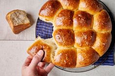 a person holding a piece of bread on top of a blue and white towel next to a loaf of bread