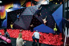 several people climbing up and down the walls in an indoor climbing area with red rocks