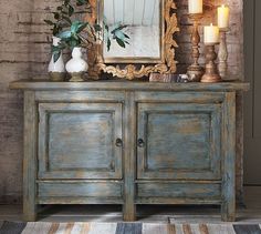 an old dresser with candles and a mirror on it in front of a brick wall