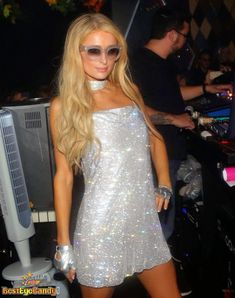 a woman in a silver dress standing next to a dj's booth at a nightclub