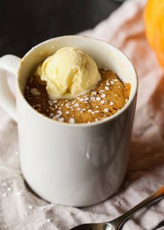 a cup with some ice cream in it on a napkin next to a spoon and an orange