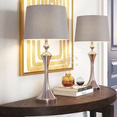 two lamps sitting on top of a wooden table next to a framed painting and lamp shade