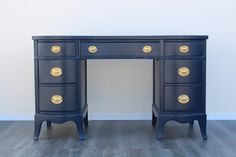 a blue desk with gold handles and drawers on it's sides, against a white wall