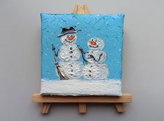 a small easel with a painting of two snowmen on it