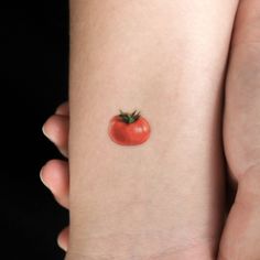 a small tomato tattoo on the back of a woman's left arm is shown