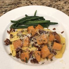 a white plate topped with food and green beans on top of a marble countertop