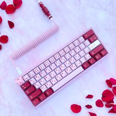 a keyboard and some red rose petals on a white surface with a pink pen next to it