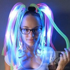 a woman with glasses and neon colored hair is posing for the camera in front of a dark background