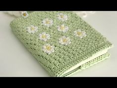 a green crocheted book with white flowers on it