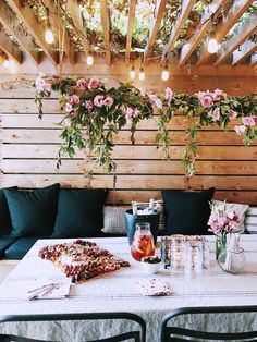 an outdoor dining area with flowers hanging from the ceiling and green cushions on the table