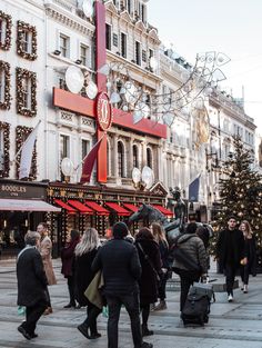 many people are walking around in front of a building with christmas decorations on the outside