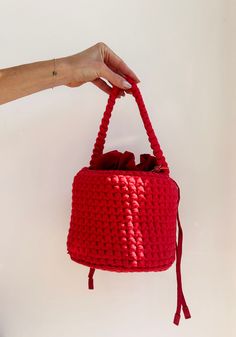 a hand holding a red crocheted bag with tassels on the handles