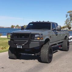 a large gray truck driving down a street next to a body of water on a sunny day