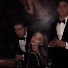 three people in tuxedos standing next to each other and one person holding a drink