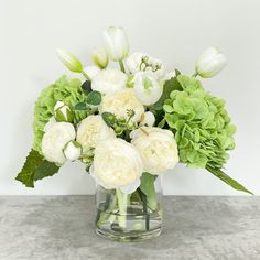 a glass vase filled with white and green flowers on top of a gray countertop