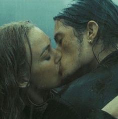 a man and woman kissing each other in front of a blue wall with water behind them