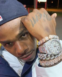 a man with tattoos on his arm and wrist wearing a watch, bracelets and a baseball cap