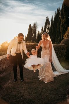 a bride and groom hold their daughter's hand as the sun sets