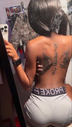 a woman with tattoos on her back looking in the mirror