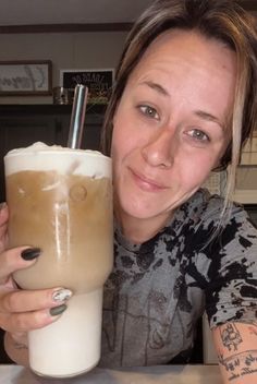 a woman holding a drink in her right hand and smiling at the camera with both hands