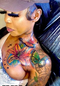 a woman with tattoos on her chest wearing a baseball cap and white tank top that has butterflies painted on it