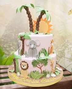 a pink cake decorated with animals and palm trees on a wooden table in front of a wall