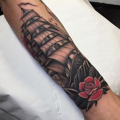 a man's arm with a ship and rose tattoo design on the left forearm