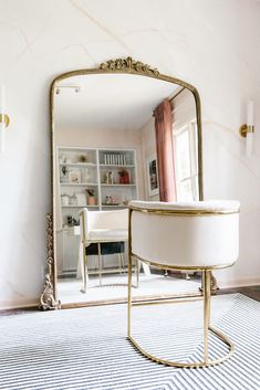 a large mirror sitting on top of a table next to a white chair in a living room