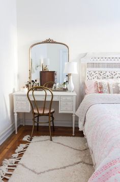 a bedroom with a white bed, desk and mirror on the wall next to it