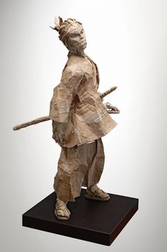 a paper mache is standing on a wooden base and holding a stick in his hand