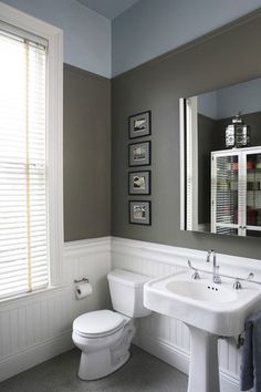 a white toilet sitting next to a sink in a bathroom under a window with pictures on the wall