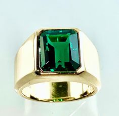 "A classic, bold, heavy ring with a bezel set Lab Grown Emerald. It is the epitome of an understated, ultra elegant, impressive Emerald Ring! The Lab Grown Emerlad is 9mm x 11mm, weighng at 5 carats. This is a ring to wear for all occasions! We are all in love with its simplicity and great style. Who we are: We are a team lead by Eden, our designer and jeweler, whose picture you see, is the talent, and the driving force of our group. We have been making custom jewelry since 1975. At our workshop Classic Jewelry With Bezel Setting And Wide Band, Classic Ring With Bezel Setting And Wide Band, Classic Wide Band Ring With Bezel Setting, Classic Emerald Ring With Smooth Bezel For Anniversary, Formal Jewelry With Bezel Setting And Wide Band, Formal Wide Band Jewelry With Bezel Setting, Classic Emerald Signet Ring With Bezel Setting, Modern Emerald Ring With Bezel Setting For Formal Events, Modern Emerald Ring With Bezel Setting For Formal Occasions