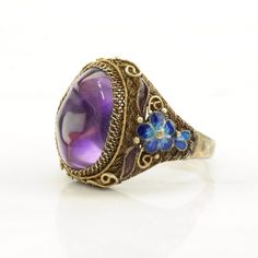 This ring is a size 9 1/2 (USA); It may not be resized Markings: 925 (Tested & guaranteed to be Sterling Silver) This ring weighs 6.8 Grams The Stone/Design is  Amethyst Enamel, Flower, Gold Tone - Natural  The Stone/Design measures 15.5 x 10.9 mm The Ring face measures 22.2 x 19.5 mm The condition of this ring is Estate, Very good, light enamel wear and one chipped enamel area, moderate to heavy patina This vintage item is circa 1950  For more vintage sterling silver rings please visit:  https://www.etsy.com/shop/SilverStarrs925?section_id=13854217 Thank you for viewing my item!  Favorite the store to get updates when items go on sale! Formal Purple Cabochon Ring, Vintage Gemstone Enamel Ring As A Gift, Vintage Enamel Gemstone Ring For Gift, Collectible Hallmarked Enamel Ring In Fine Jewelry Style, Purple Cabochon Amethyst Wedding Ring, Vintage Purple Round Jewelry, Vintage Enamel Jewelry With Gemstone, Vintage Enamel Gemstone Jewelry, Fine Jewelry Purple Cabochon