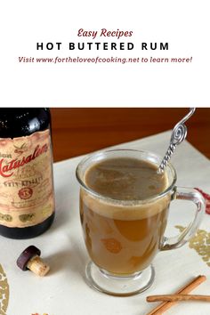 hot buttered rum in a glass mug next to cinnamon sticks and an empty bottle