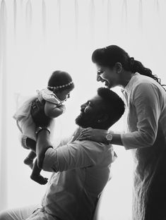 a man and woman holding a baby in front of a window