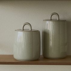 two ceramic containers sitting on top of a wooden shelf