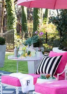 a patio with pink furniture and an umbrella over the table that has drinks on it