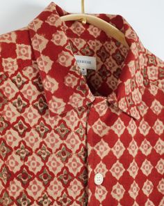 a red and white shirt hanging on a wooden hanger with a button down collar