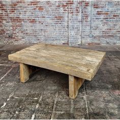 a wooden table sitting on top of a cement floor next to a brick wall in an old building