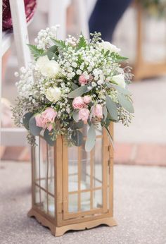 a vase filled with white and pink flowers on top of a wooden stand next to a person