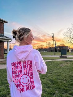 a woman in a pink hoodie is standing on the grass with her back to the camera