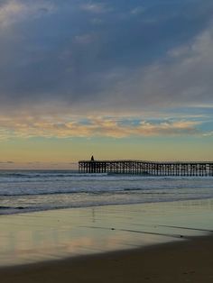 a person walking on the beach with a surfboard in front of an ocean pier