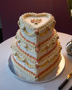 a wedding cake that is shaped like a heart on top of a table next to utensils