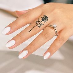 a woman's hand with a ring and flower tattoo on her left thumb, next to a white manicure