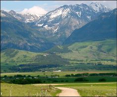 a dirt road in the middle of a grassy field with mountains in the background and snow - capped peaks