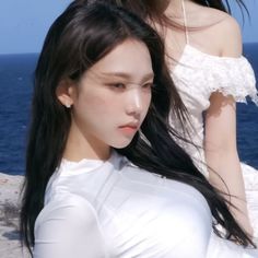 two beautiful young women standing next to each other near the ocean with long black hair